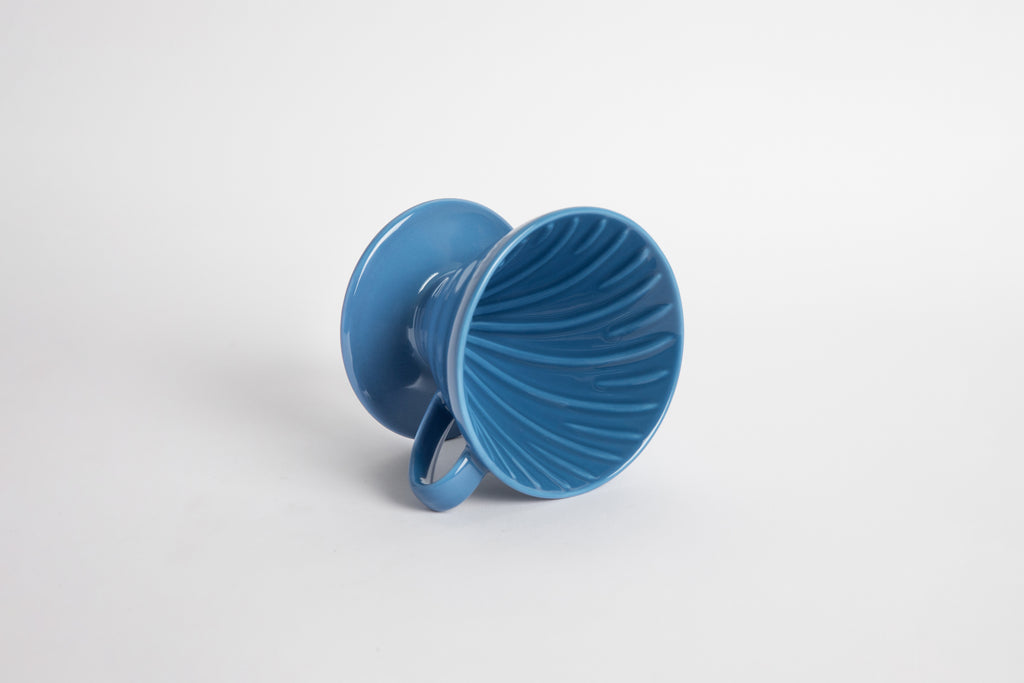 Blue colored 60 degree cone shaped ceramic coffee dripper with handle and round base. Spiral ribbed on the inside cone. Set on white background