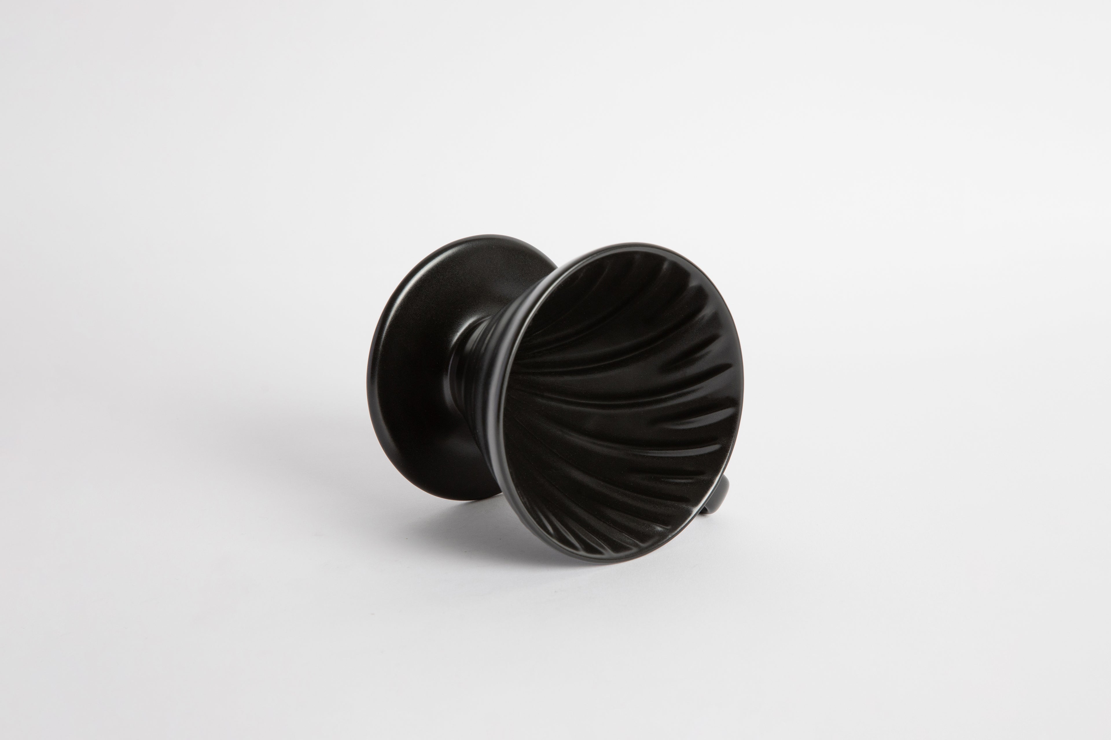 Black colored 60 degree cone shaped ceramic coffee dripper with handle and round base. Spiral ribbed on the inside cone. Set on white background