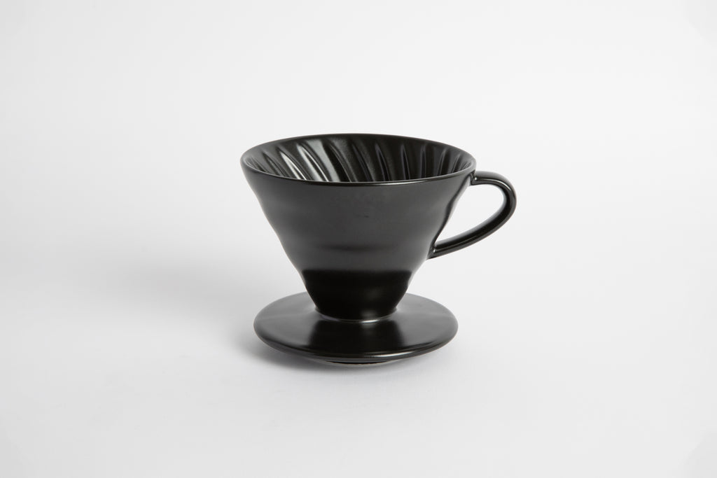 Black colored 60 degree cone shaped ceramic coffee dripper with handle and round base. Spiral ribbed on the inside cone. Set on white background