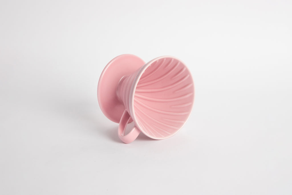 Pink colored 60 degree cone shaped ceramic coffee dripper with handle and round base. Spiral ribbed on the inside cone. Set on white background