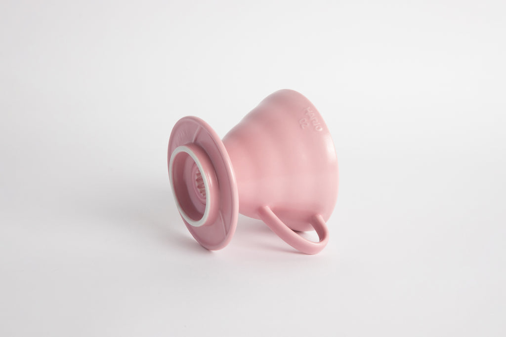 Pink colored 60 degree cone shaped ceramic coffee dripper with handle and round base. Set on white background