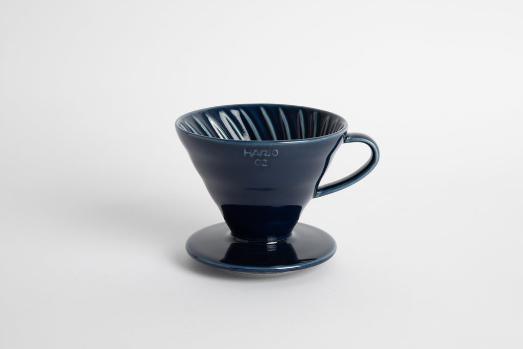Navy colored 60 degree cone shaped ceramic coffee dripper with handle and round base. Spiral ribbed on the inside cone. Set on white background