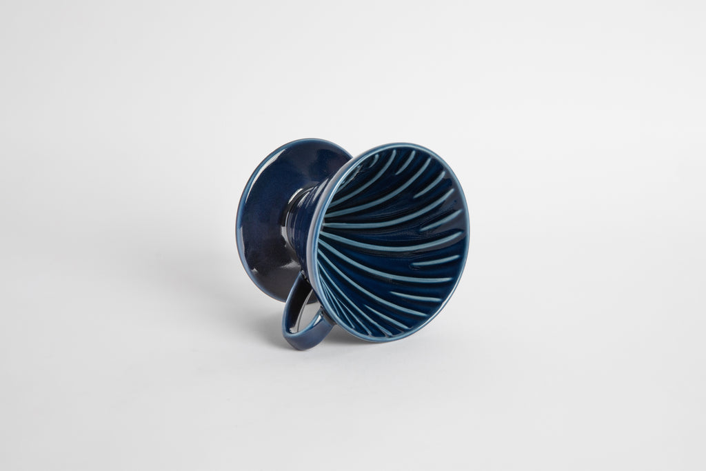 Navy colored 60 degree cone shaped ceramic coffee dripper with handle and round base. Spiral ribbed on the inside cone. Set on white background