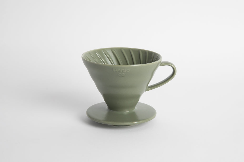 "Oil Green" sage colored 60 degree cone shaped ceramic coffee dripper with handle and round base. Spiral ribbed on the inside cone. Set on white background