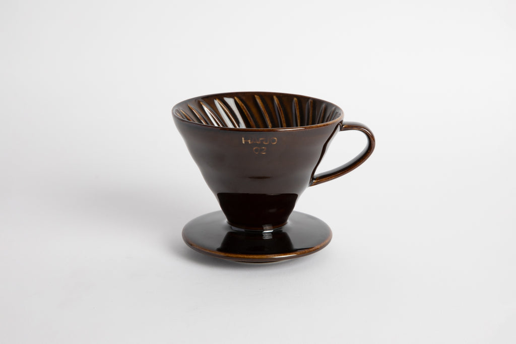 "Saddle" Dark Brown 60 degree cone shaped ceramic coffee dripper with handle and round base. Spiral ribbed inside of the cone. Set on white background