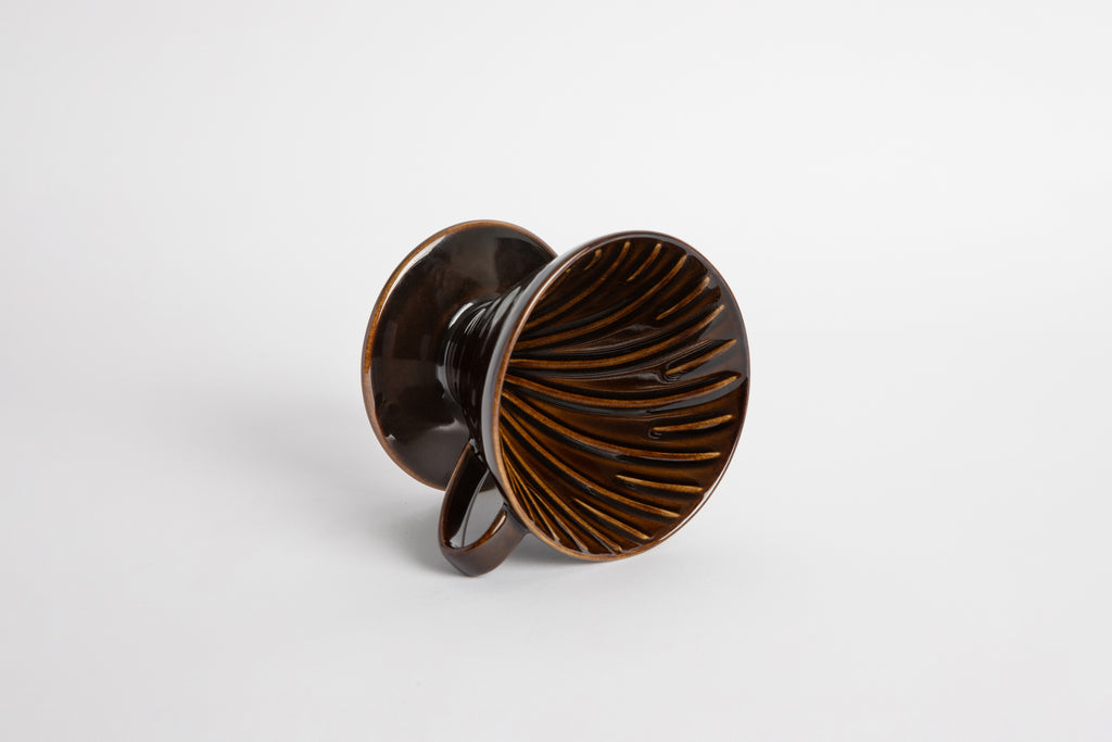 "Saddle" Dark Brown 60 degree cone shaped ceramic coffee dripper with handle and round base. Spiral ribbed inside of the cone. Set on white background
