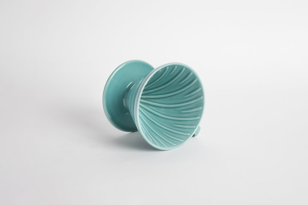 Turquoise 60 degree cone shaped ceramic coffee dripper with handle and round base. Ribbed on the inside cone. Set on white background