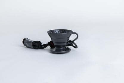 black cone shaped plastic coffee dripper  cup with handle and round base.  with a black rope tied on the handle Set on white background