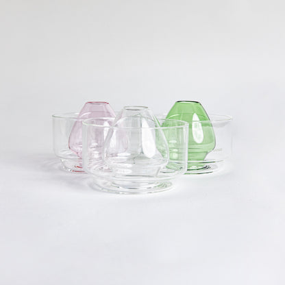 Three side by side images of a dome-shaped in the colors clear, pink and green clear glass matcha whisk holder with a smooth, tapered form, placed inside a clear glass base. Displayed on a white background