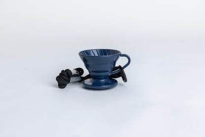 navy blue cone shaped plastic coffee dripper  cup with handle and round base.  with a black rope tied on the handle Set on white background