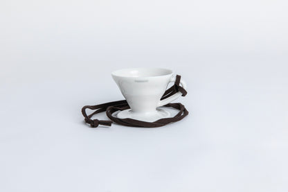 white cone shaped ceramic coffee dripper  cup with handle and round base.  with a brown rope tied on the handle Set on white background
