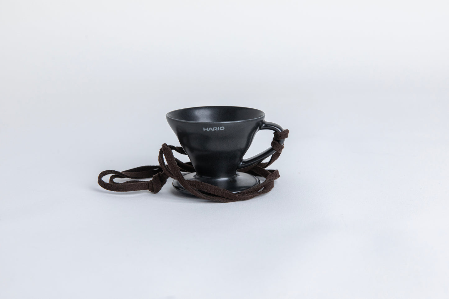 matte black cone shaped ceramic coffee dripper  cup with handle and round base.  with a brown rope tied on the handle Set on white background