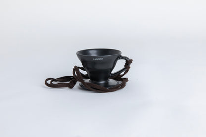 matte black cone shaped ceramic coffee dripper  cup with handle and round base.  with a brown rope tied on the handle Set on white background