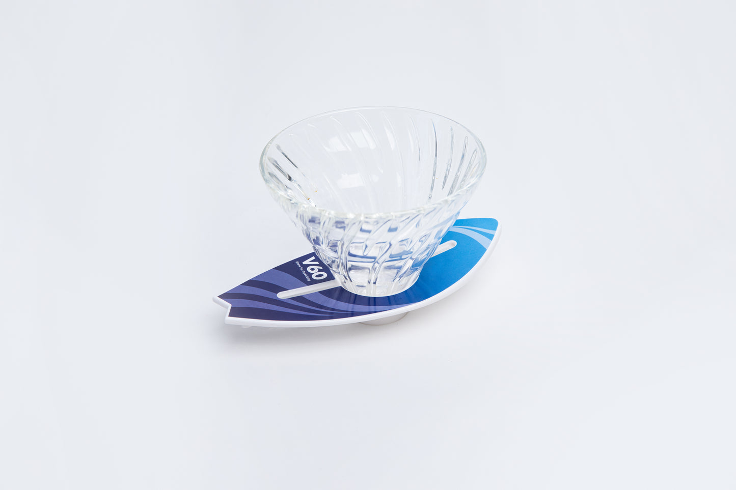 Clear glass v60 dripper on a blue and white surfboard base against a light gray background