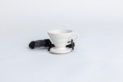white cone shaped plastic coffee dripper  cup with handle and round base.  with a black rope tied on the handle Set on white background