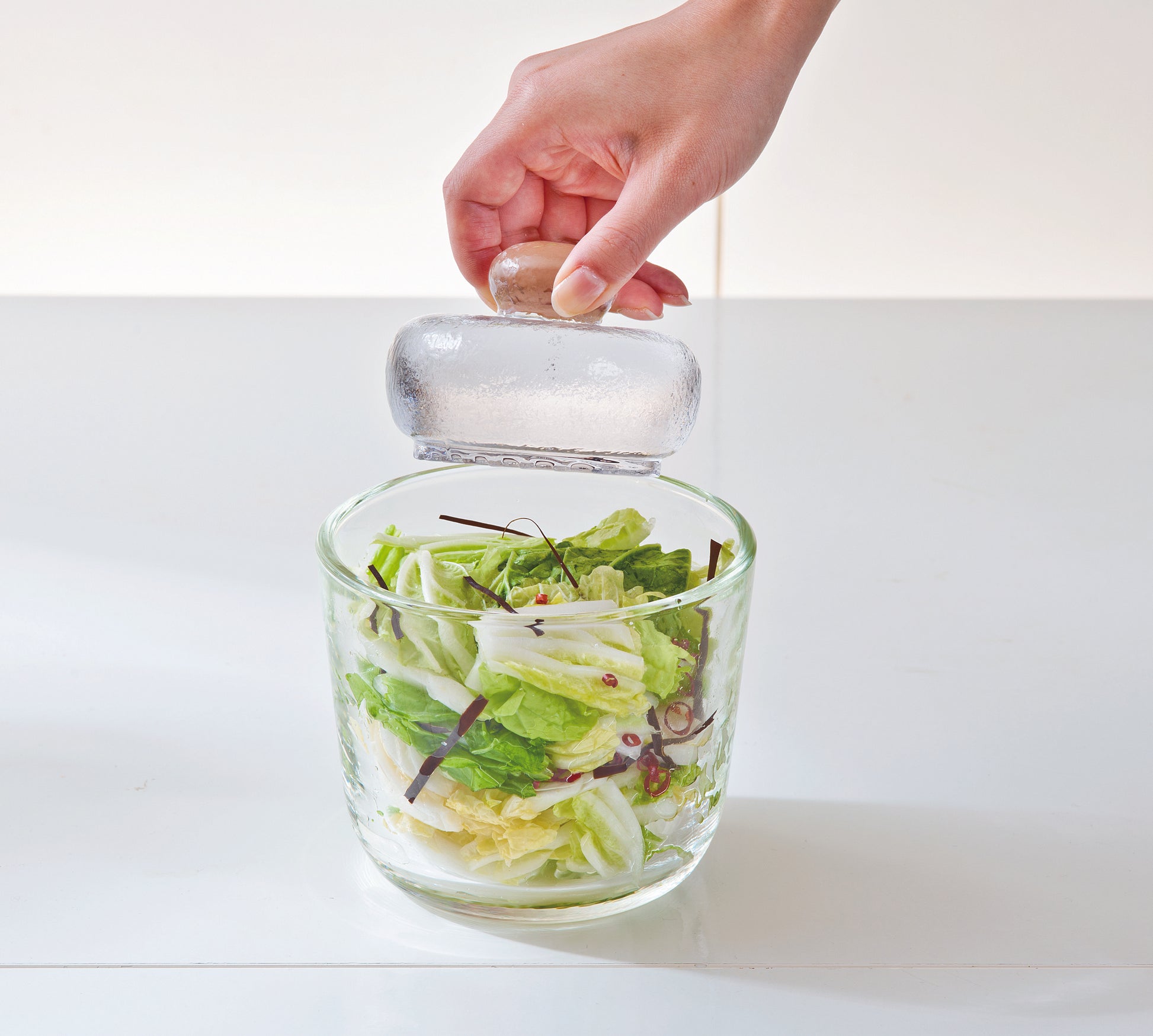 Woman's hand holding the knob of weighted glass stone above glass salting bowl with salad inside.