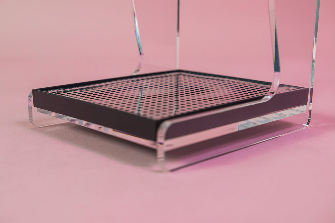 Close up of the chrome screen in the black plastic drip tray on a clear acrylic stand with hole for cone dripper and black plastic drip with chrome screen on a pink backdrop.