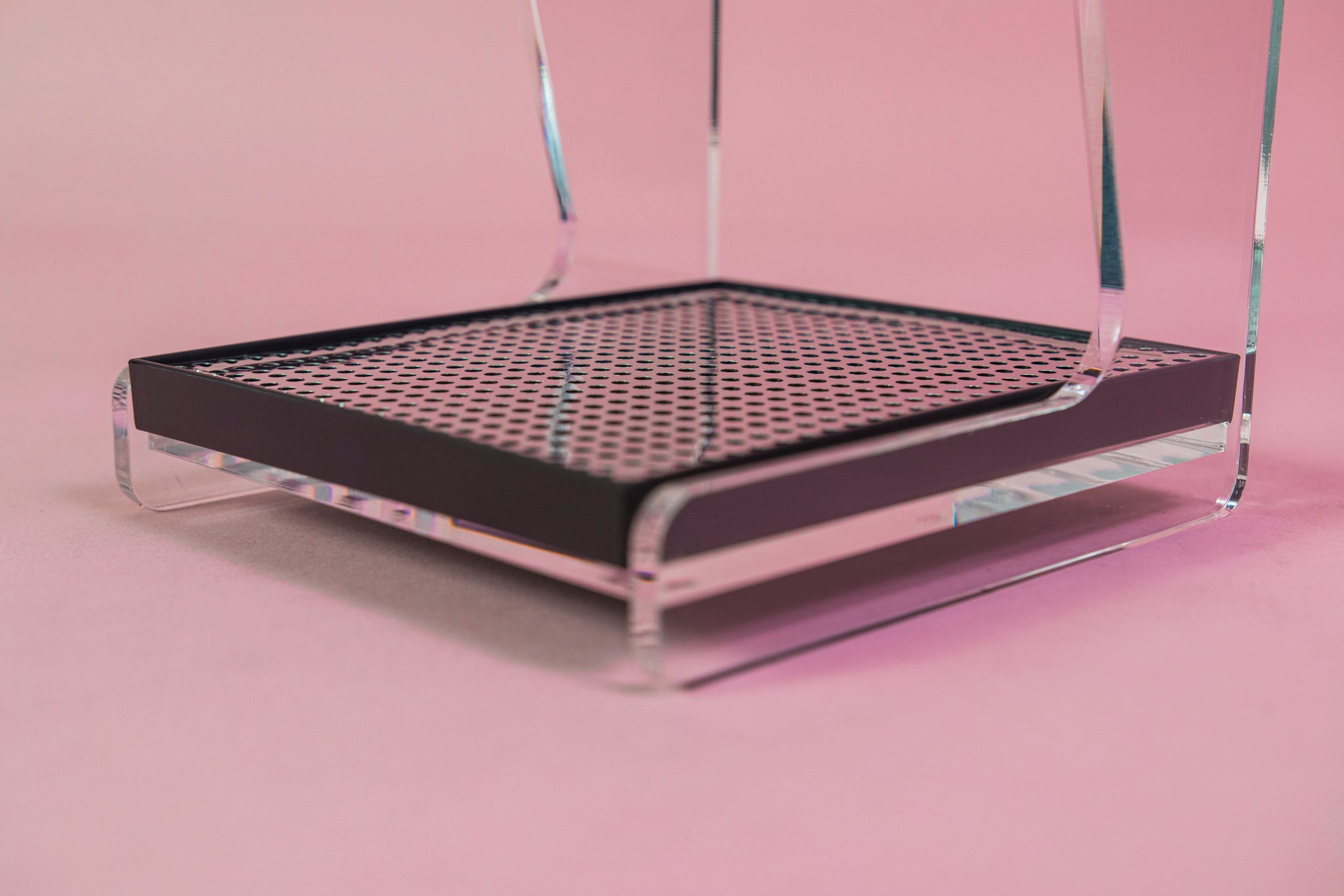 Close up of the chrome screen in the black plastic drip tray on a clear acrylic stand with hole for cone dripper and black plastic drip with chrome screen on a pink backdrop.