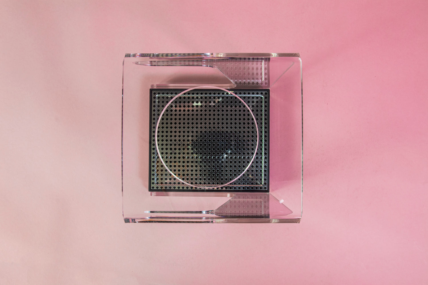 Top view of a clear acrylic stand with hole for cone dripper and black plastic drip with chrome screen on a pink backdrop.