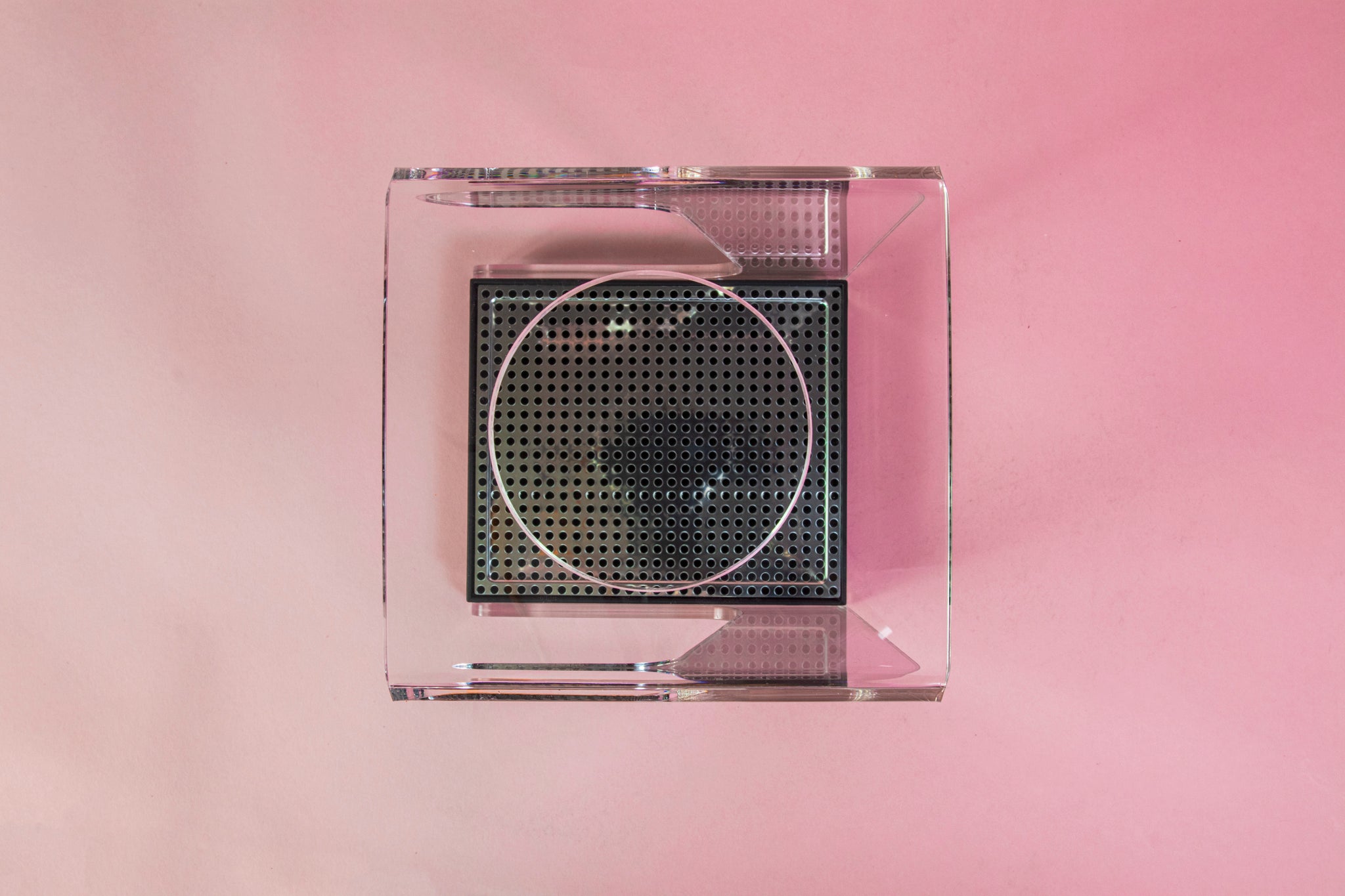 Top view of a clear acrylic stand with hole for cone dripper and black plastic drip with chrome screen on a pink backdrop.