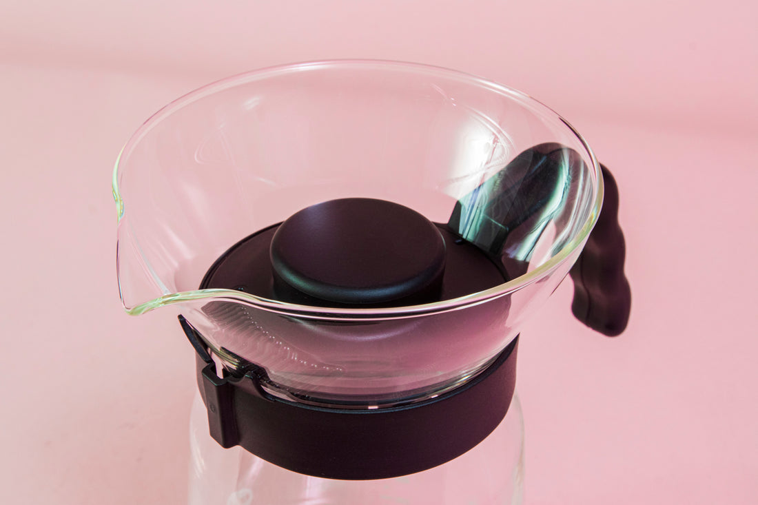 Close up of spout and lid on a tall glass coffee decanter with black plastic handle with a frosted plastic insert and black plastic cone dripper on top with black plastic server lid.