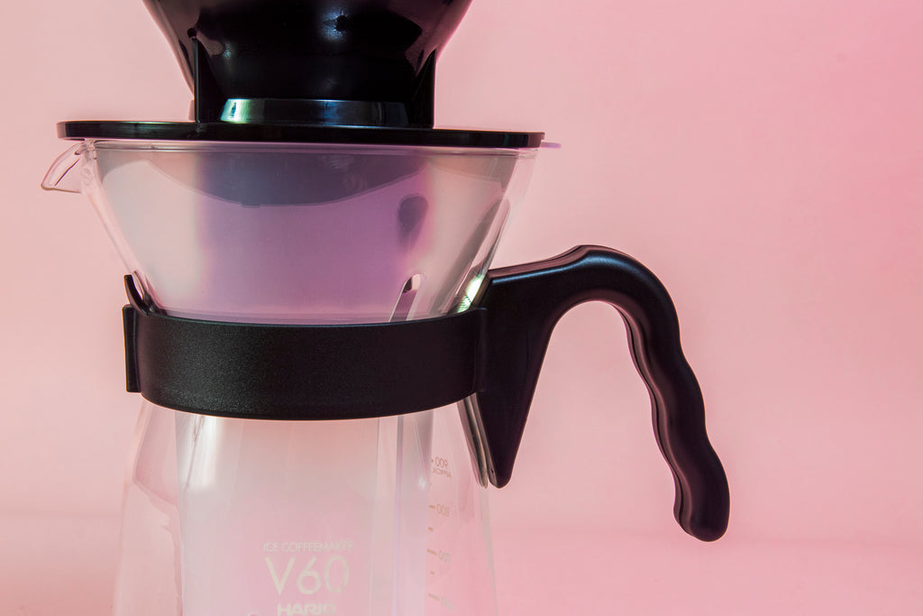 Close up of collar on a tall glass coffee decanter with black plastic handle with a frosted plastic insert and black plastic cone dripper on top with black plastic server lid.