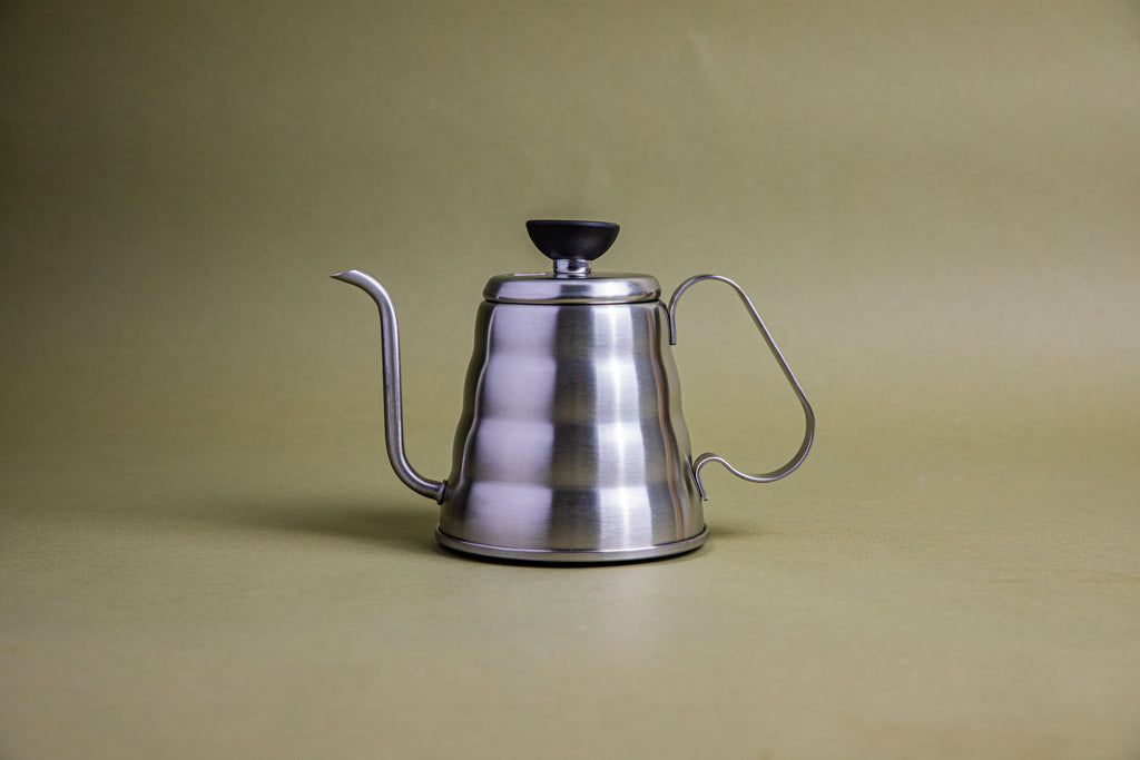 Stainless steel, beehive-shaped kettle with gooseneck spout, stainless steel lid with black plastic lid knob, and full stainless steel handle set against an earth-tone background.