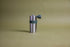 Stainless steel cylindrically shaped coffee mill cannister with forest green silicone band holding stainless steel handle with plastic knob. Set against an earth-tone background.