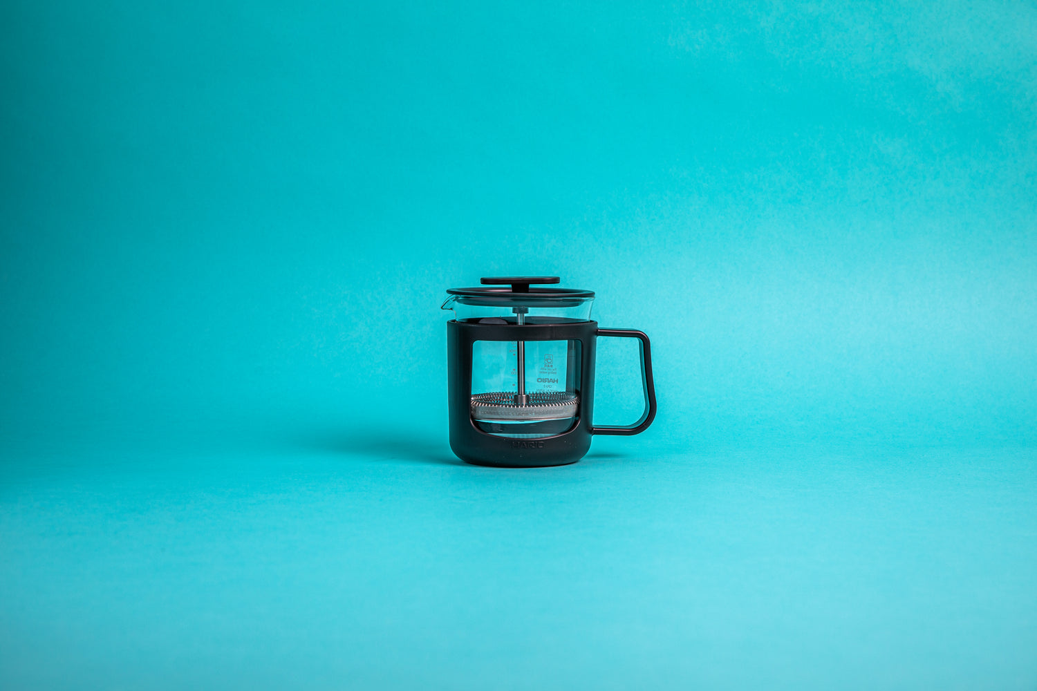 Coffee press featuring a glass pitcher with fluted spout, stainless steel mesh filter with pole, and a black plastic lid, knob, holder, and handle. Set against a blue background.