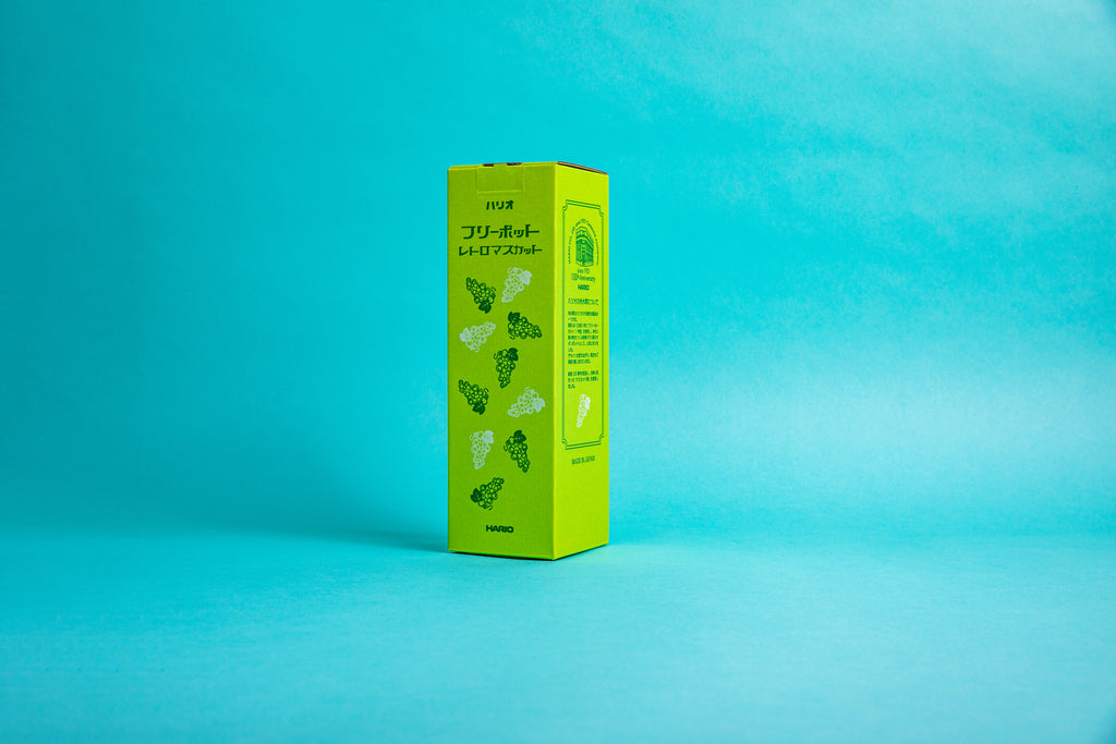Tall, narrow, yellow packaging box with green and white grape pattern on one side and description in Japanese of the company Hario on the other. Set against a blue background.