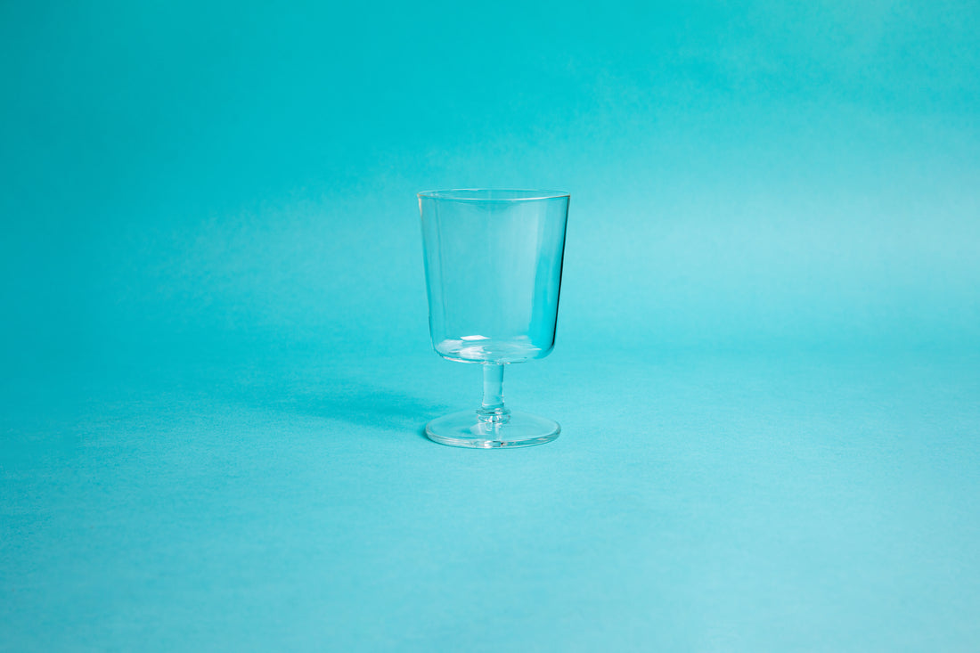 Heatproof square glass goblet with glass stem and foot. Set on blue background.