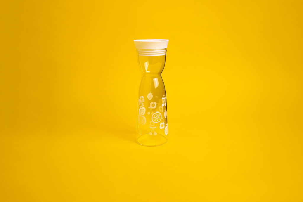 Hourglass shaped glass with white flower etching. Topped with a white silicone cap. Set on a yellow background.