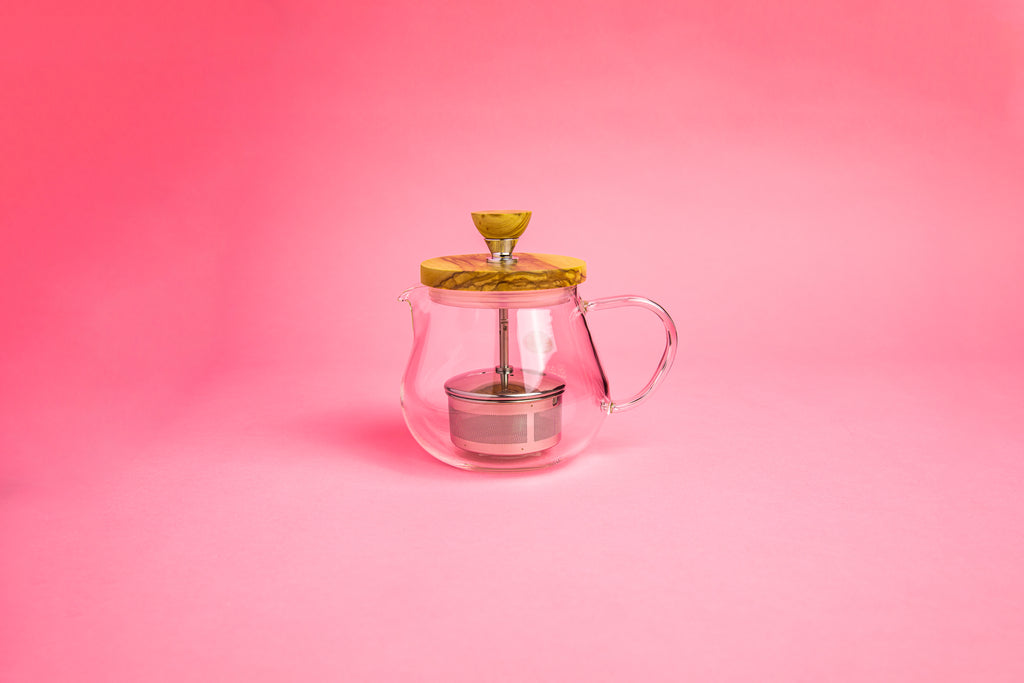 Glass teapot with glass handle. Olive wood lid and knob. Stainless steel plunger with metal tea filter basket .  set on pink gradient background