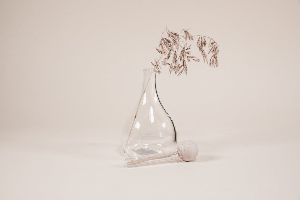 Tear drop shaped glass diffuser with natural wood wand, round knob, and diffusing plant.