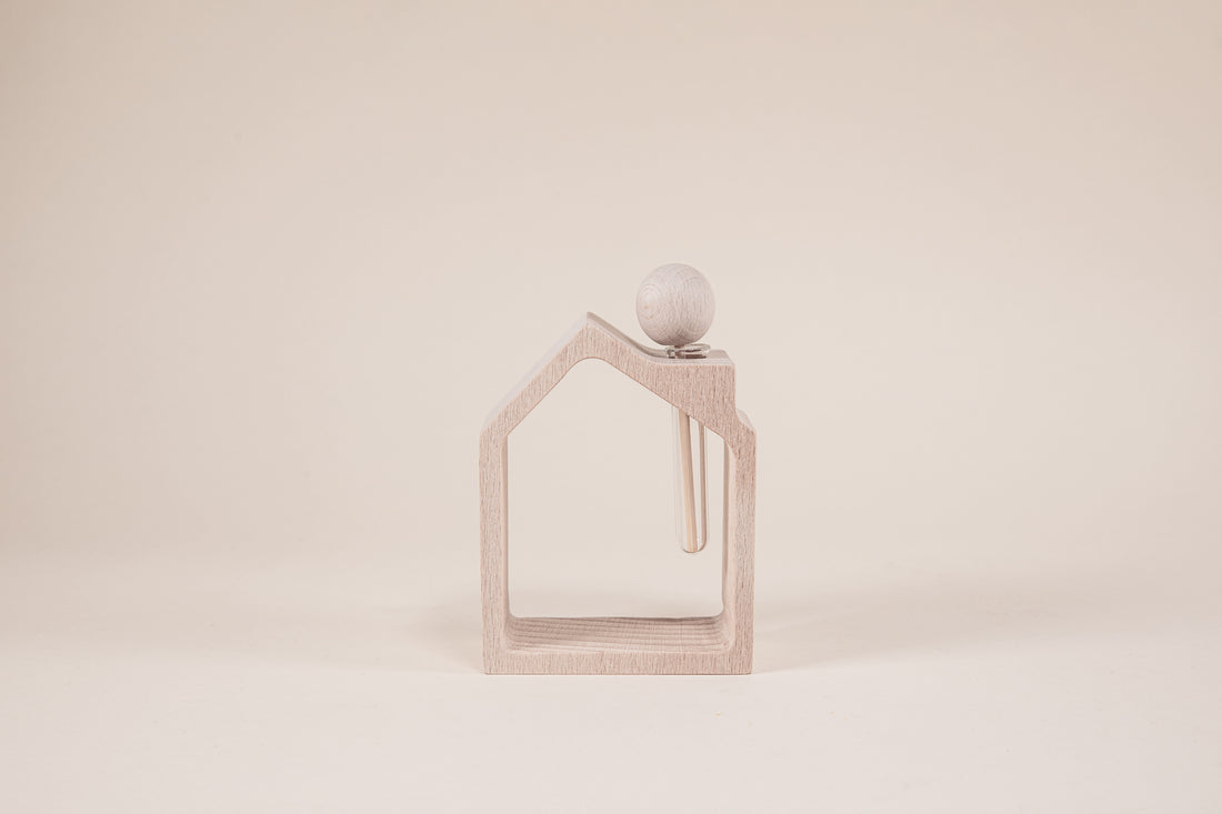 Wooden house frame with wooden stick shaped like a popsicle inside a glass vile on a light brown background.