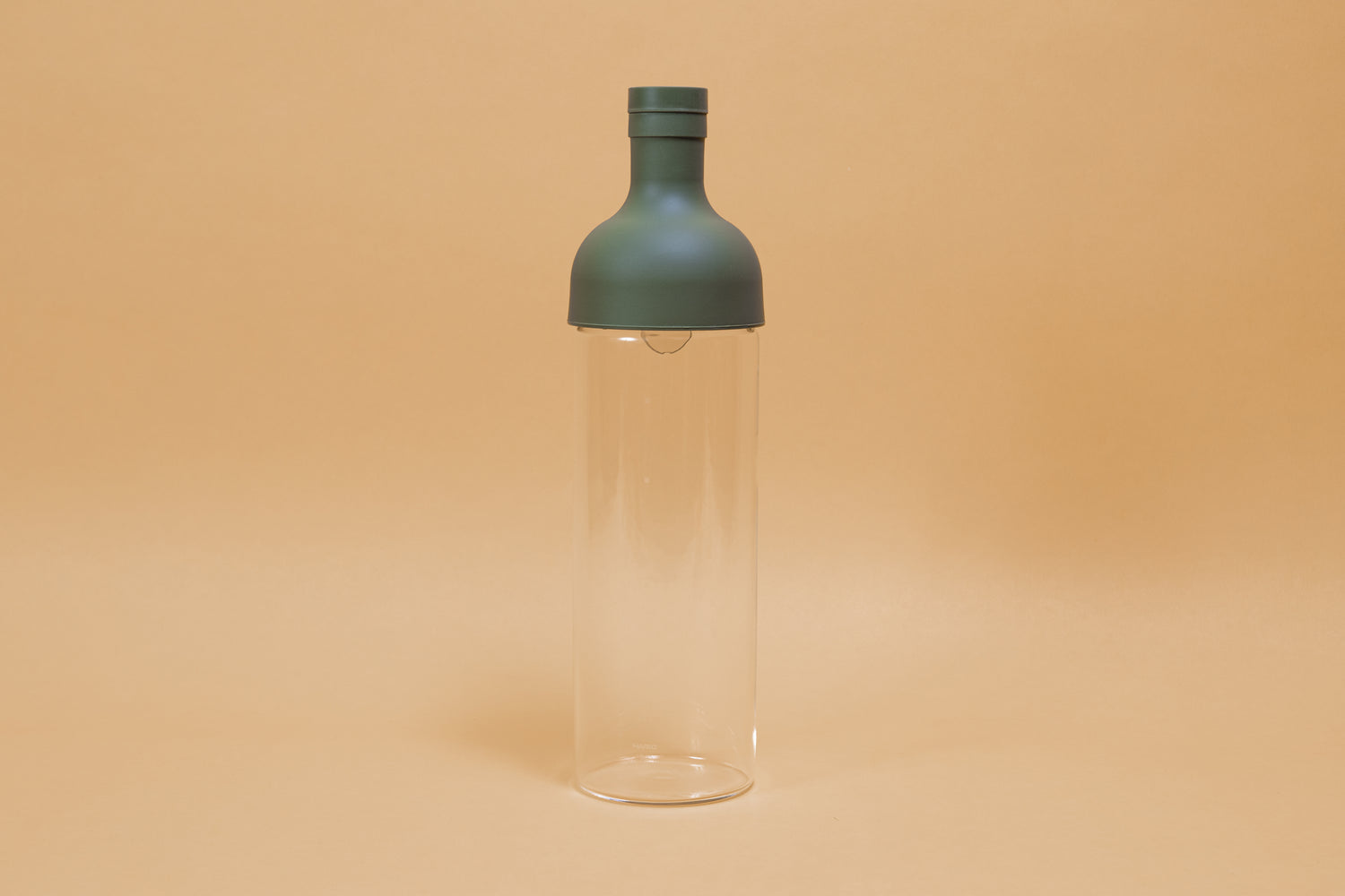 Tall glass container with green rubber wine bottle shaped top on an orange backdrop.
