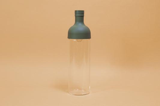 Tall glass container with green rubber wine bottle shaped top on an orange backdrop.