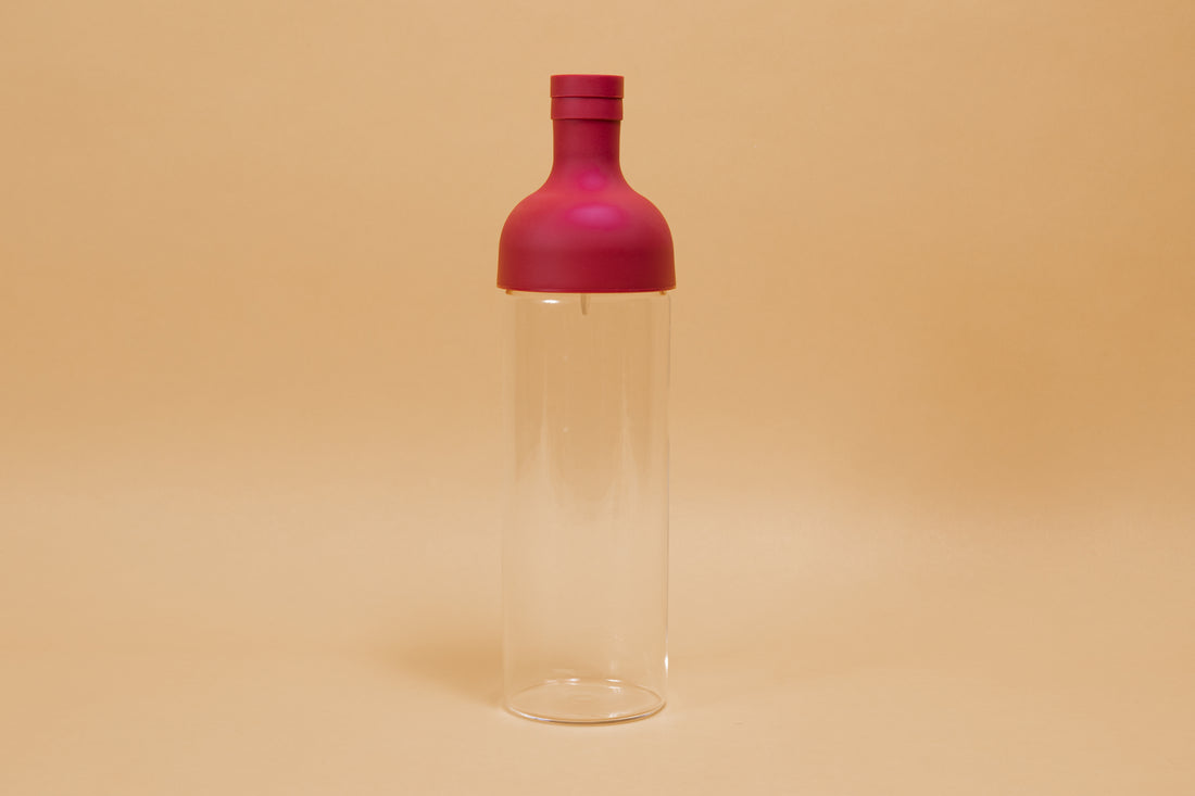 Tall glass container with red rubber wine bottle shaped top on an orange backdrop.