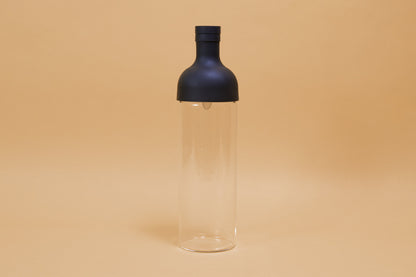 Tall glass container with black rubber wine bottle shaped top on an orange backdrop.