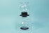 Globulous glass tear brewer and metal mesh filter with clear plastic lid atop a black rubber base with plastic lever switch on a clear acrylic stand above an all glass bulbous server with handle