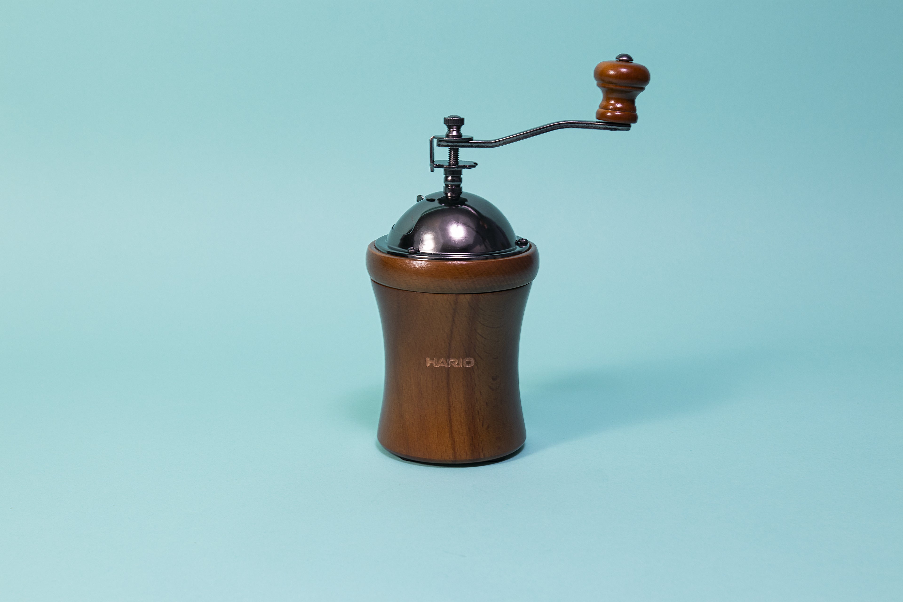 Round wooden grinder tapered in the middle with dark metal dome on top with wooden knobbed metal handle