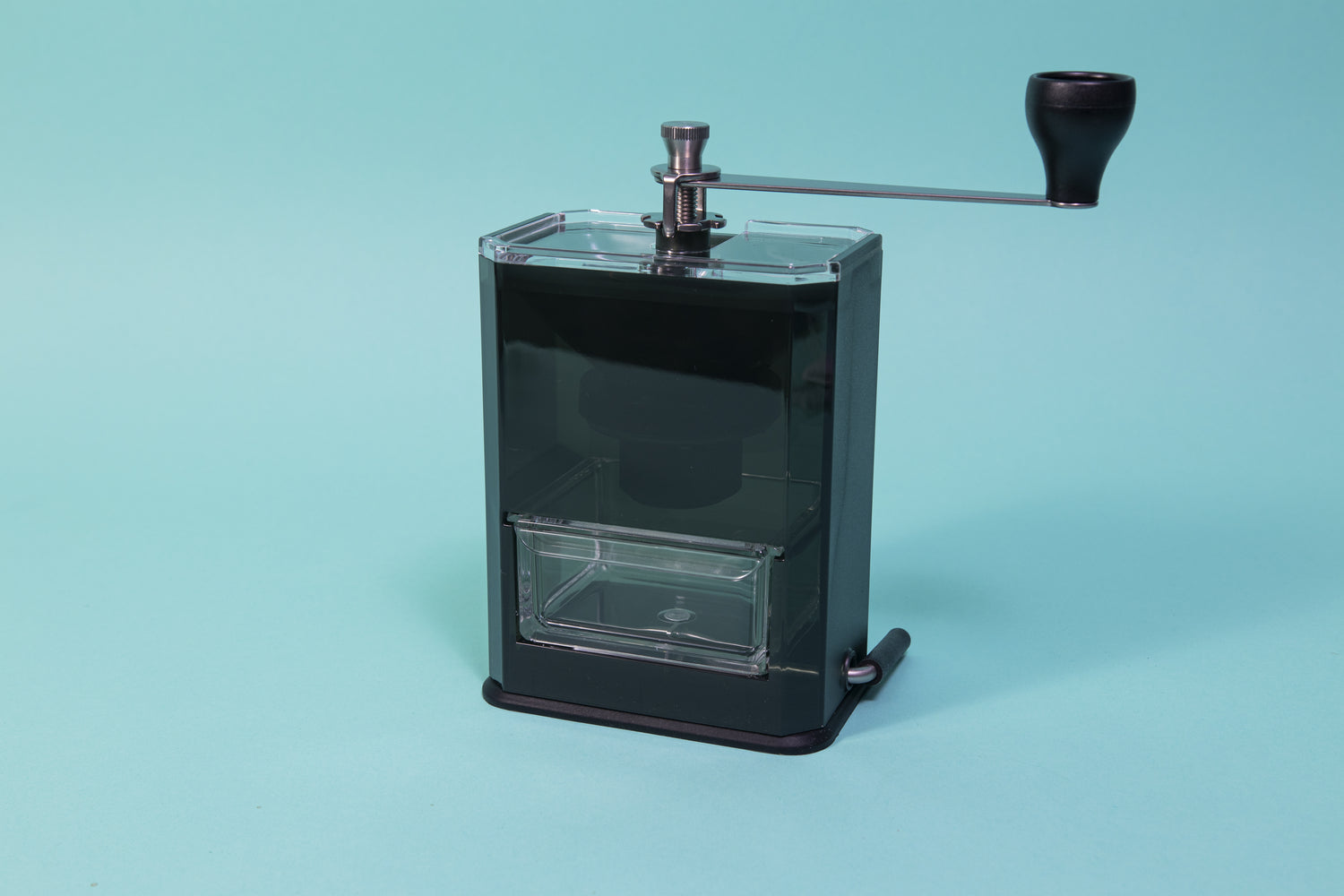 Dark black acrylic monolithic grinder body with clear drawer and  grinding handle on top, and smaller lever on bottom.