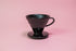 Black conical ceramic coffee dripper with handle and round base.