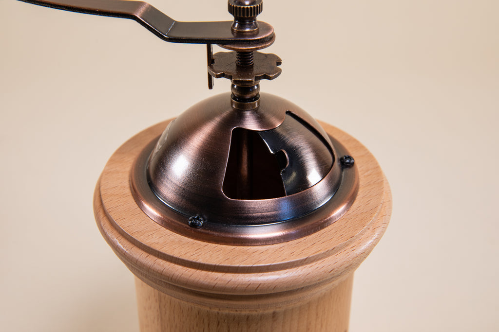 Close up of open sliding metal hopper gate on a cylindrical wood grinder with bronze metal grinder hopper, with sliding metal gate, and handle with wood knob
