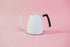 Matte white metal gooseneck kettle with white lid knob and black rubber handle cover.