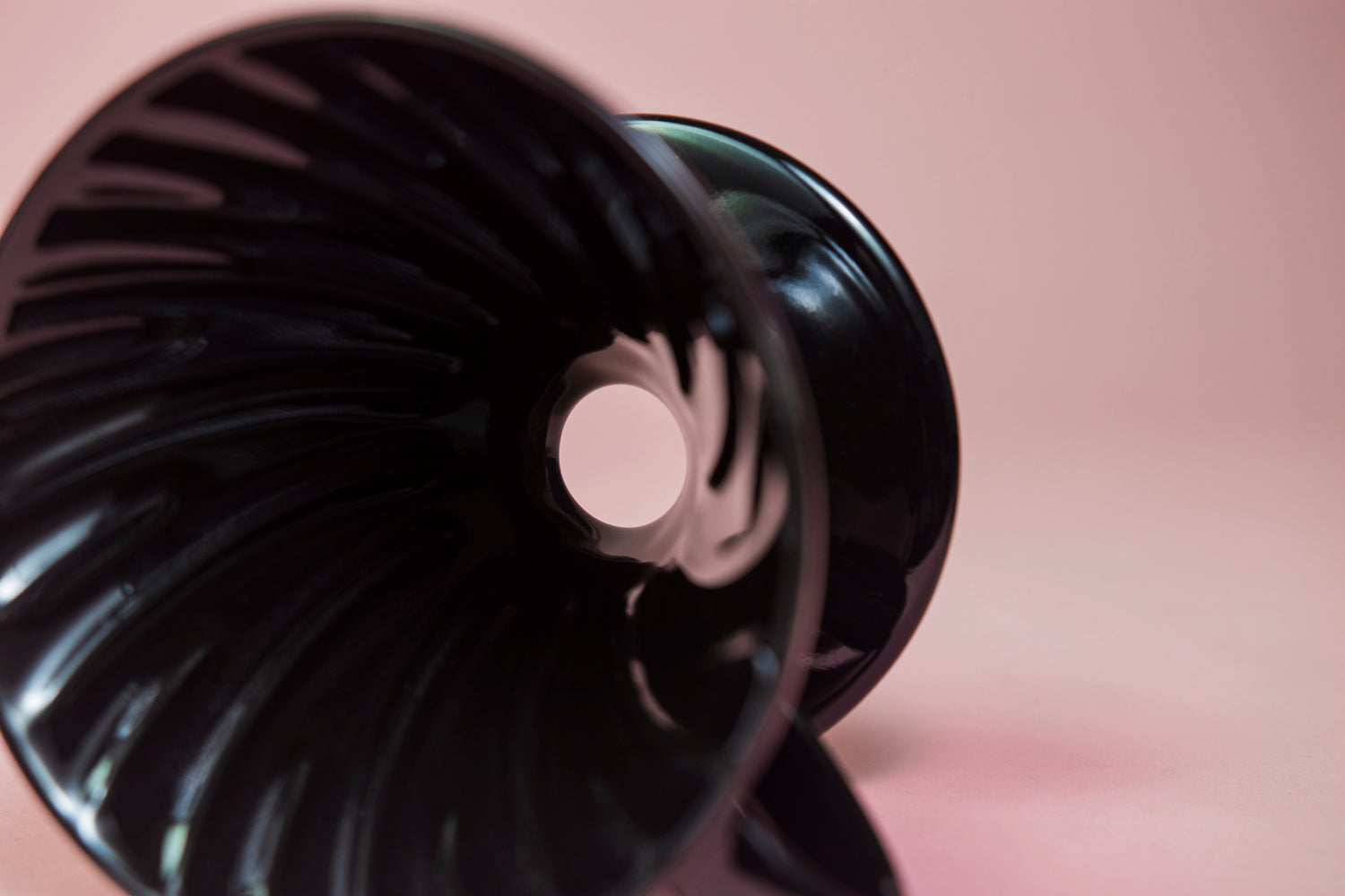 Black conical ceramic coffee dripper with handle and round base lying on its side showing the smooth drip hole