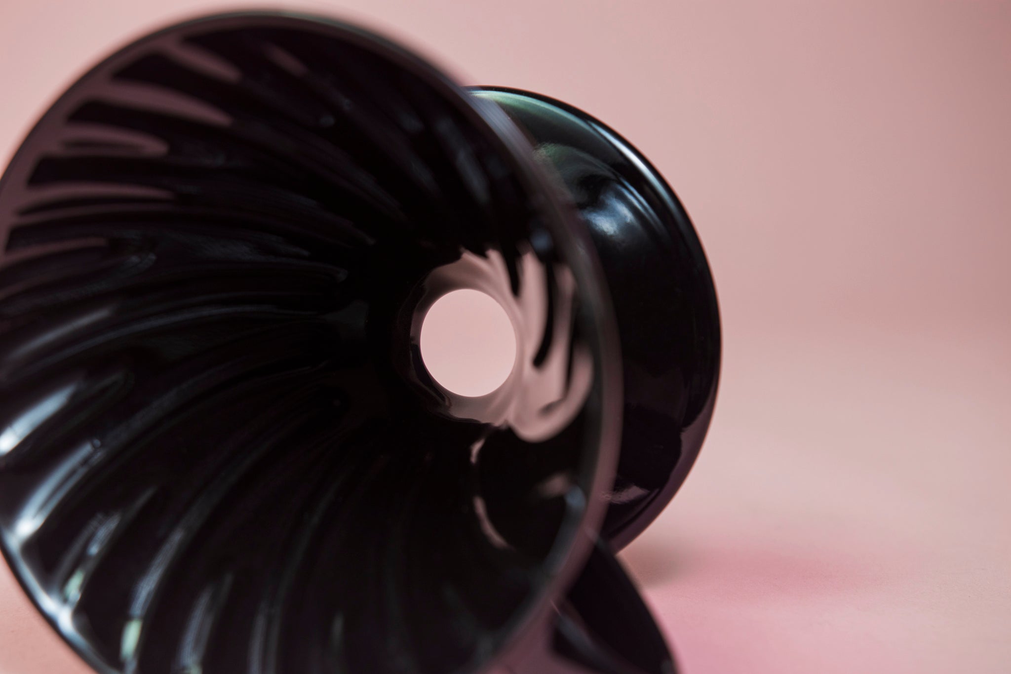 Black conical ceramic coffee dripper with handle and round base lying on its side showing the smooth drip hole