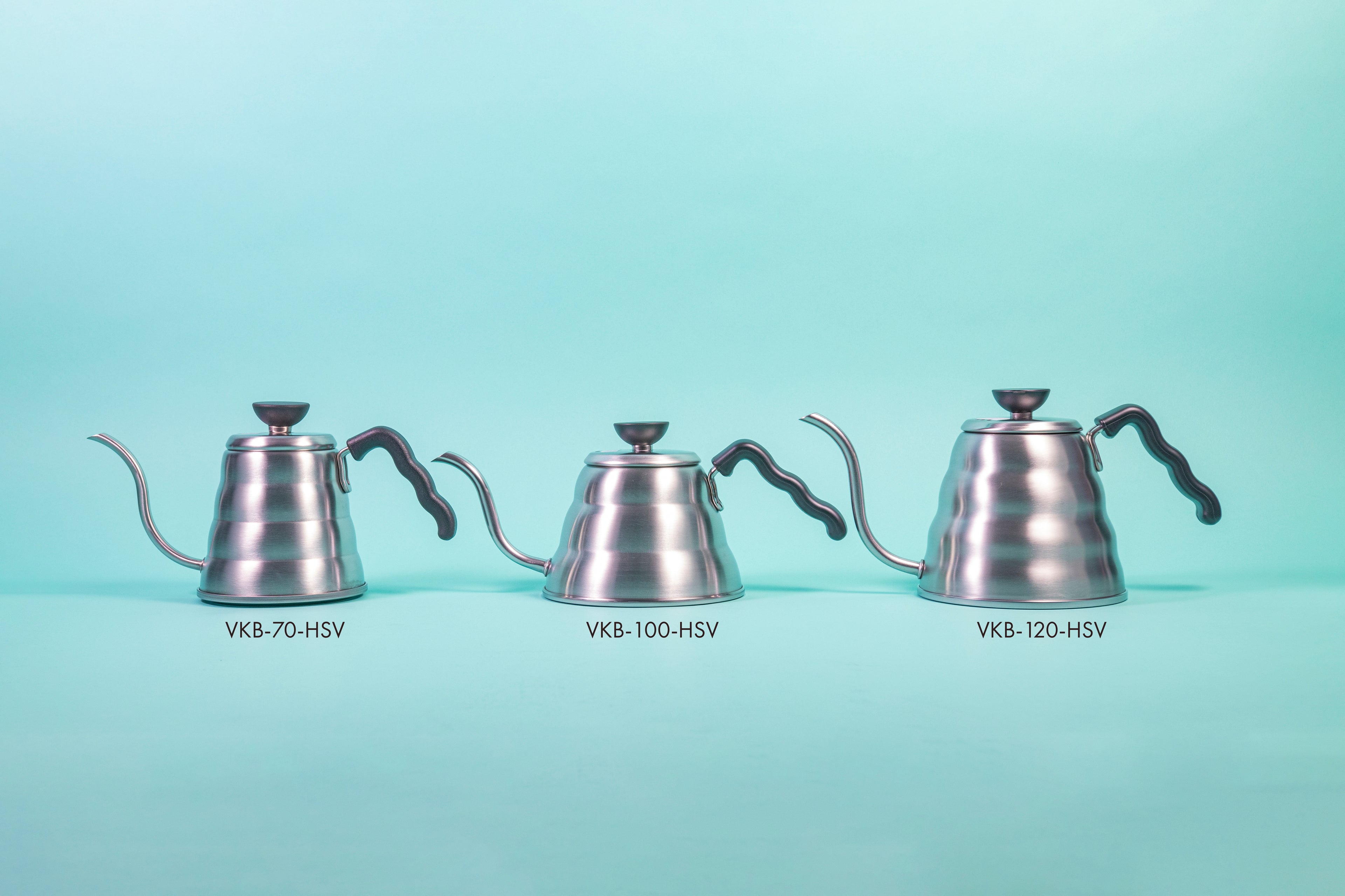 Three silver beehive-shaped stainless steel kettles of varying sizeswith wave-shaped black plastic handles and round black plastic lid knobs with flat tops set against a light blue background.
