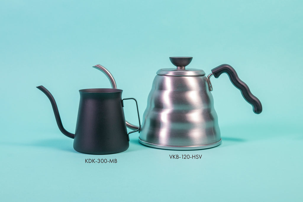All black metal kettle with flared top, gooseneck spout, handle, and next to a silver beehive-shaped kettle with black plastic waved handle and round black lid knob with flat top. Set against a blue background.