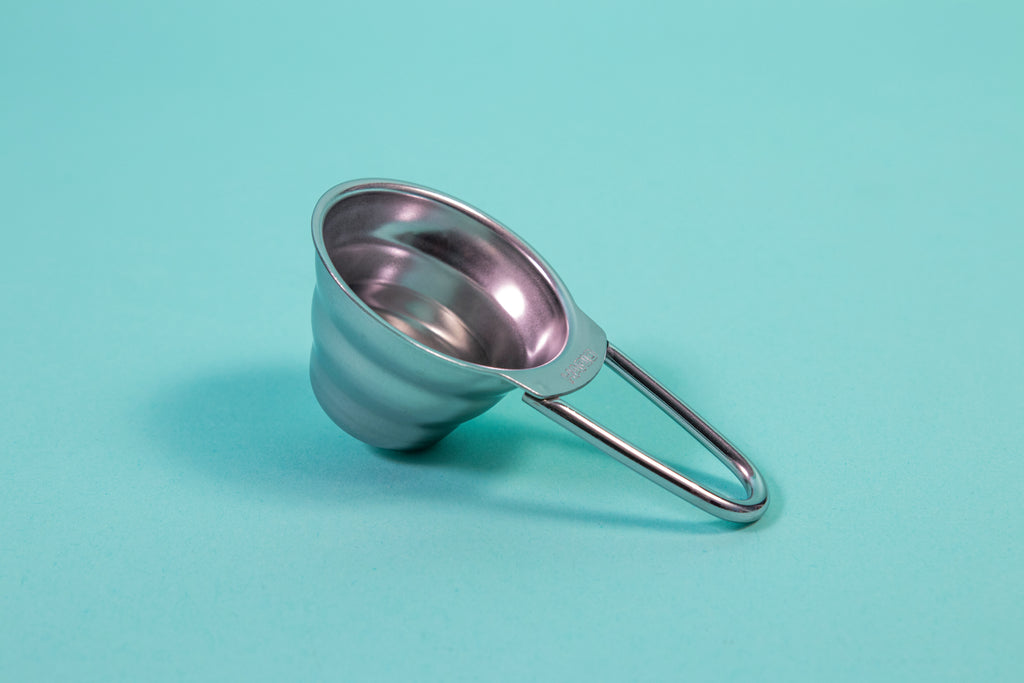 Stainless steel beehive shaped measuring spoon with bezier shaped open air handle on a blue background.